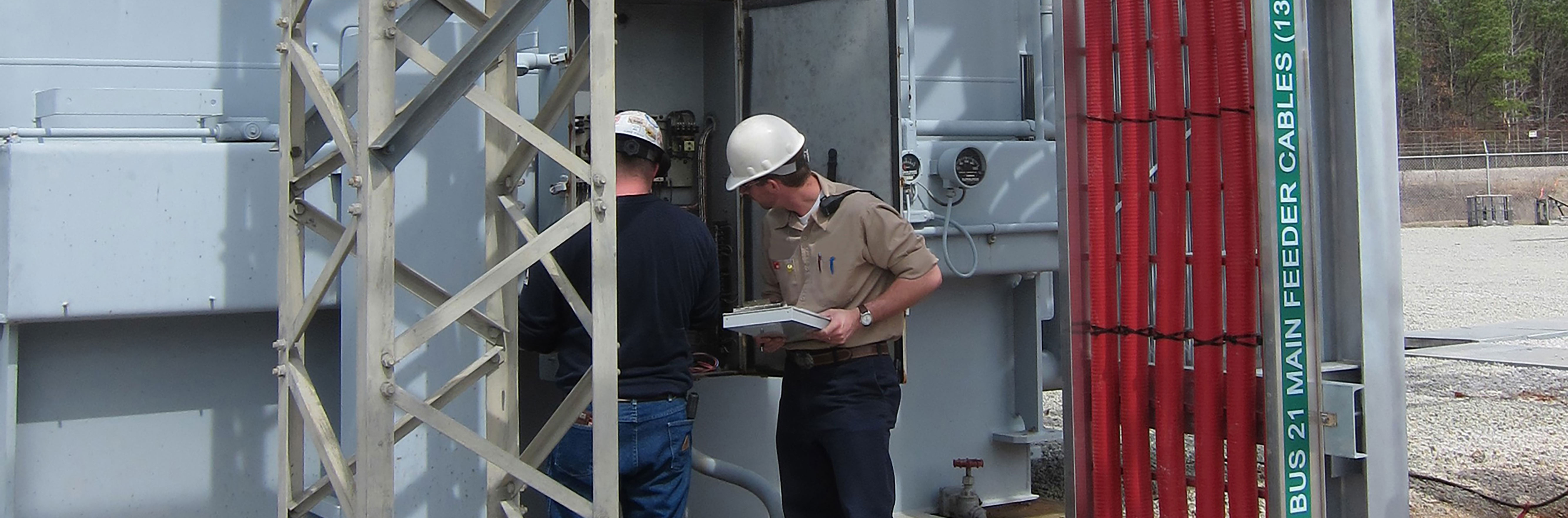 two technicians in hard hats inspecting industrial plant power controls as part of regular maintenance services