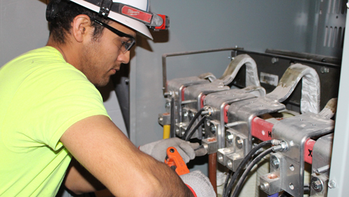 an electrician with hard hat and safety glasses connecting industrial circuit breakers